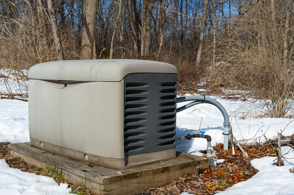 Residential standby generator on a concrete pad with snow on ground.