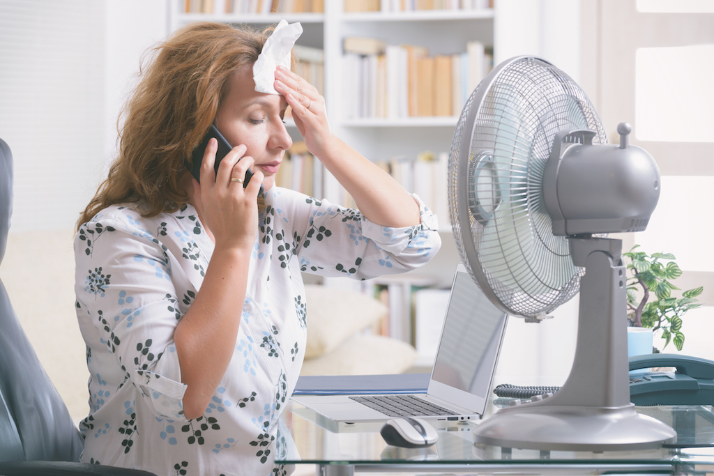 Woman suffers from heat while working in the office and tries to cool off by the fan. Needs a ceiling fan.