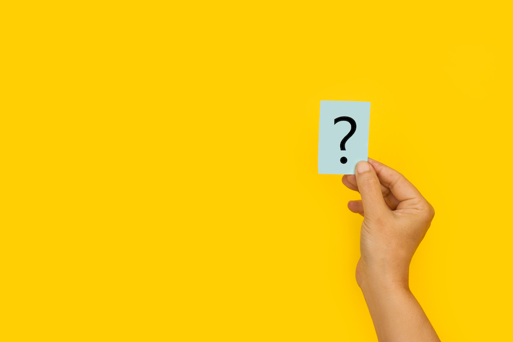 Yellow background with person holding a question mark sticker. Representing FAQs about smoke detectors.
