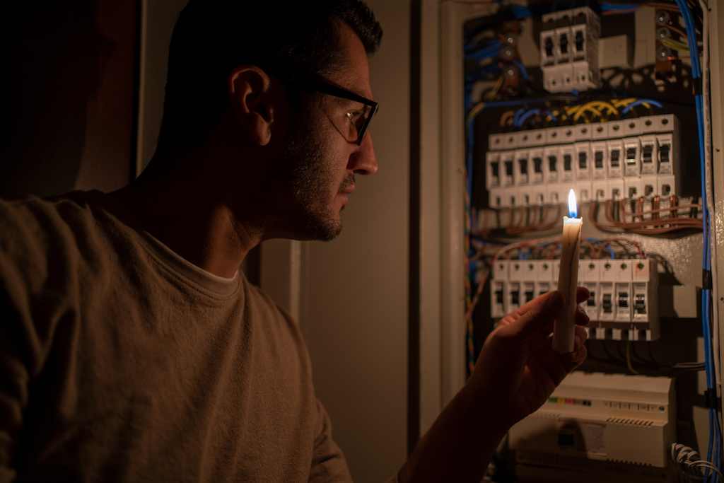 Man holding a candle up to electrical subpanel during power outage. 