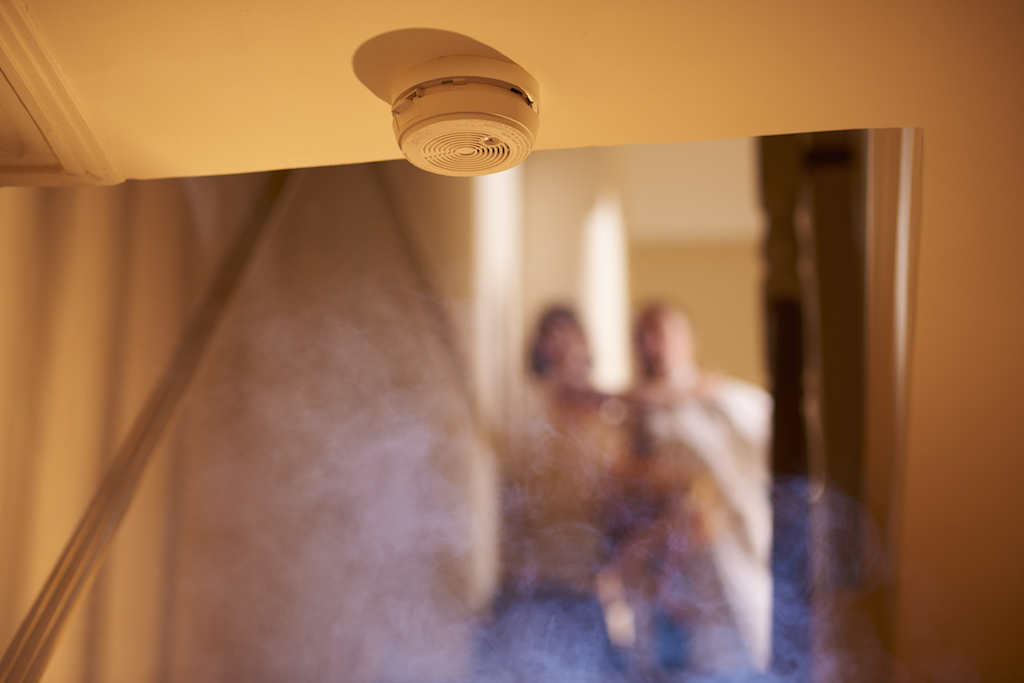 Smoke detector with smoke and a blurred family in the background.