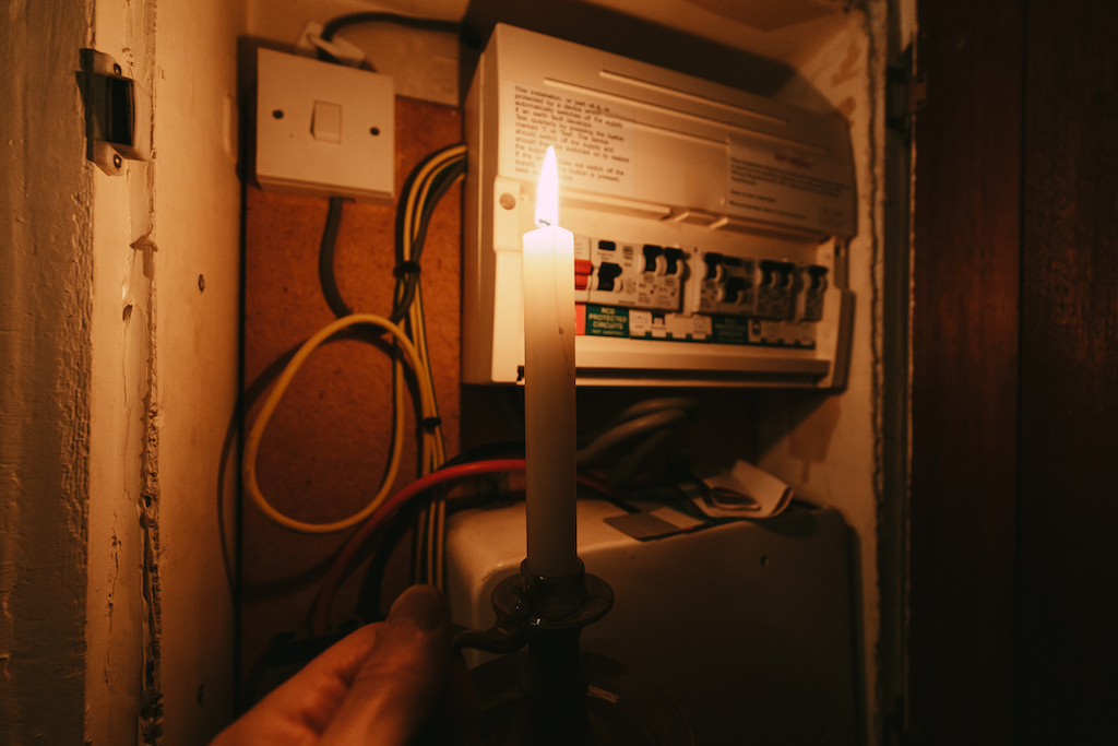 Person holding a candle to their residential fuse box during an unexpected power outage. In need of a general electrician.