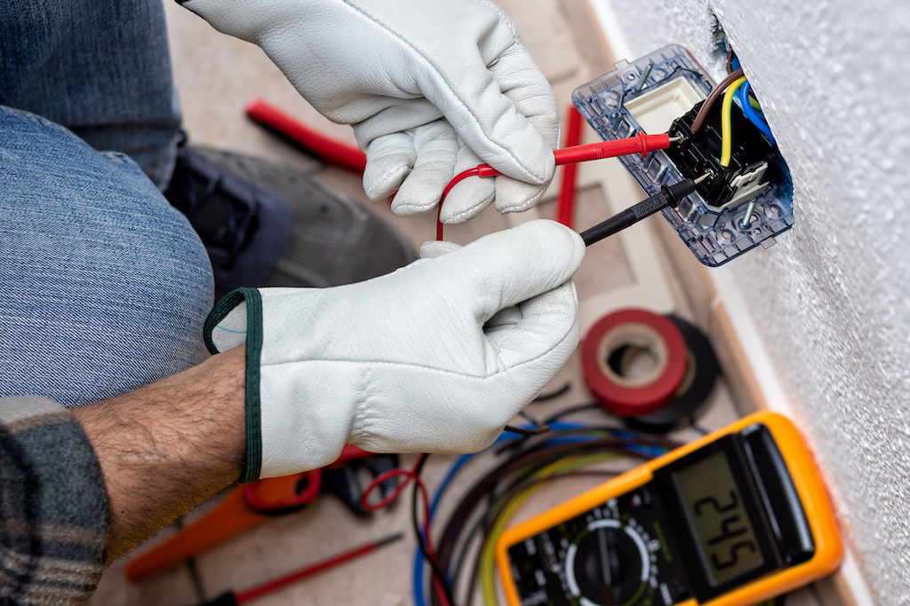 Electrician working safely with a device measuring the voltage in the electrical system. Emergency Electrical Services.
