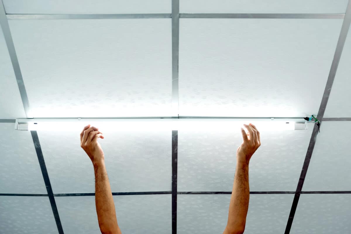 Close-up of a man's hand installing a long LED Conversion bulb on the ceiling.
